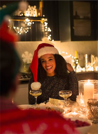 simsearch:6113-08659542,k - Smiling woman wearing Santa hat at candlelight Christmas dinner party Fotografie stock - Premium Royalty-Free, Codice: 6113-08659598