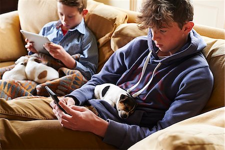 Boys using digital tablet and cell phone with puppies sleeping in laps Stock Photo - Premium Royalty-Free, Code: 6113-08659674