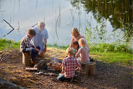 smiling senior people talking family - Grandparents and grandchildren enjoying campfire at lakeside Stock Photo - Premium Royalty-Free, Code: 6113-08698074