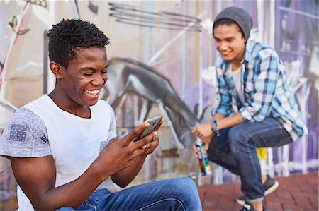 Smiling teenage boys hanging out texting and spray painting graffiti on urban wall Stock Photo - Premium Royalty-Free, Code: 6113-08698248