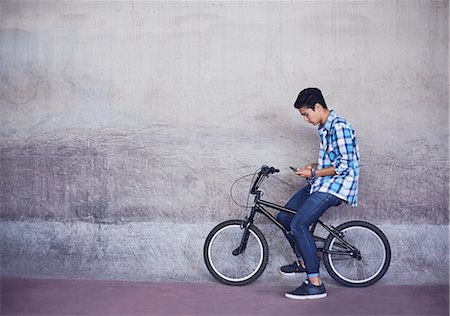 simsearch:6116-07085094,k - Teenage boy texting on BMX bicycle at wall Foto de stock - Sin royalties Premium, Código: 6113-08698224