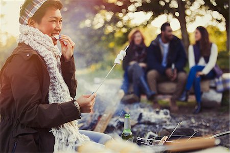 Smiling woman eating roasted marshmallows at campfire Stock Photo - Premium Royalty-Free, Code: 6113-08743407