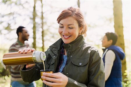 Smiling woman pouring coffee from insulated drink container in woods Stock Photo - Premium Royalty-Free, Code: 6113-08743418