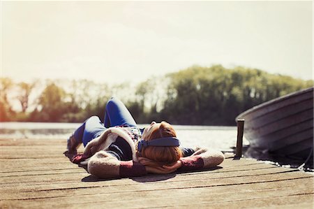 simsearch:649-09002373,k - Woman relaxing laying on dock listening to music with headphones at sunny lakeside Stock Photo - Premium Royalty-Free, Code: 6113-08743420