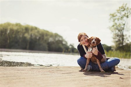 Portrait smiling woman hugging dog on sunny lakeside dock Stock Photo - Premium Royalty-Free, Code: 6113-08743546