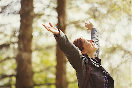 Exuberant woman hiking in sunny woods with head back and arms raised Stock Photo - Premium Royalty-Free, Code: 6113-08743548