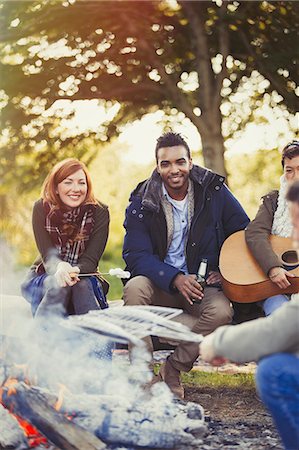 Smiling friends roasting marshmallows and drinking beer at campfire Foto de stock - Sin royalties Premium, Código: 6113-08743595