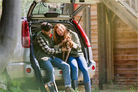 dog with people - Couple petting dog at back of car outside sunny cabin Foto de stock - Sin royalties Premium, Código: 6113-08743526