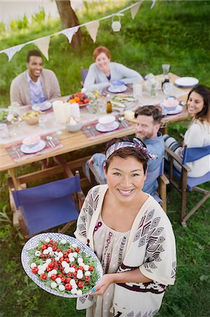 people standing at a dinner table - Portrait smiling woman serving Caprese salad to friends at garden party table Stock Photo - Premium Royalty-Free, Code: 6113-08743528