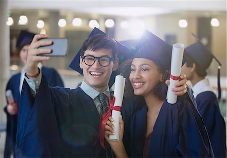 simsearch:6113-07906519,k - College graduates in cap and gown holding diplomas posing for selfie Foto de stock - Sin royalties Premium, Código: 6113-08769675