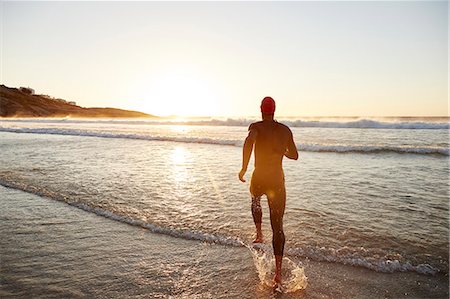 sunrise man back - Male triathlete swimmer in wet suit running into ocean surf at sunrise Stock Photo - Premium Royalty-Free, Code: 6113-08769772