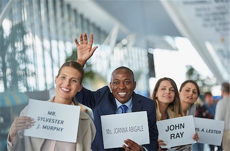 Chauffeurs with welcome signs smiling and waving in a row at airport Stock Photo - Premium Royalty-Free, Code: 6113-08784165