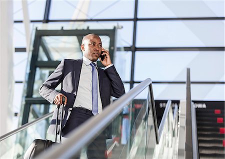 Businessman talking on cell phone on airport escalator Stock Photo - Premium Royalty-Free, Code: 6113-08784196