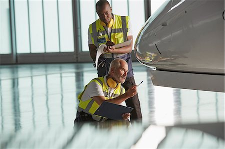 simsearch:6113-08784253,k - Airport ground crew workers examining airplane in hangar Foto de stock - Sin royalties Premium, Código: 6113-08784271