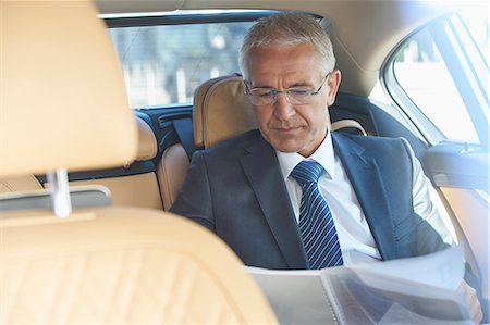 Businessman reviewing paperwork in back seat of town car Photographie de stock - Premium Libres de Droits, Code: 6113-08784235