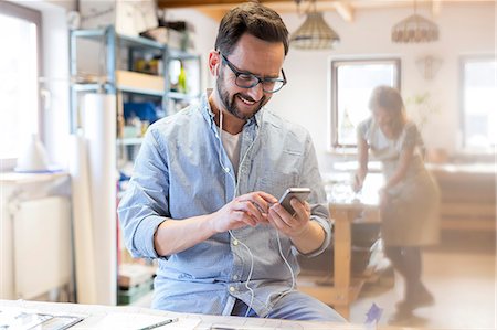 simsearch:6113-08985870,k - Smiling artist listening to music with earbuds and mp3 player in studio Stock Photo - Premium Royalty-Free, Code: 6113-08784383