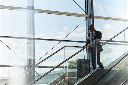 Businessman with suitcase talking on cell phone on airport escalator Stock Photo - Premium Royalty-Free, Code: 6113-08784313