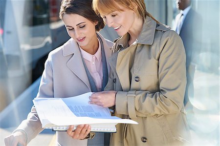 Businesswomen reading paperwork on sunny train station platform Stock Photo - Premium Royalty-Free, Code: 6113-08784324