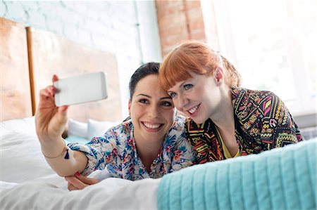 Smiling women taking selfie with camera phone laying on bed Stock Photo - Premium Royalty-Free, Code: 6113-08784442