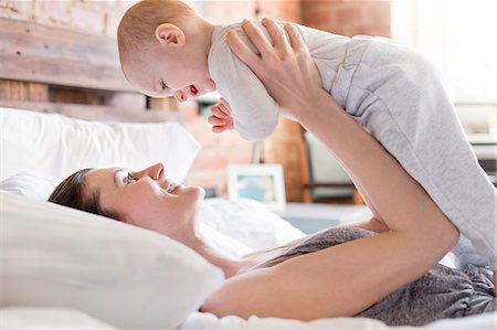 Smiling mother holding baby daughter overhead on bed Stock Photo - Premium Royalty-Free, Code: 6113-08784406