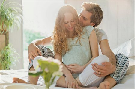 Affectionate pregnant couple kissing in pajamas on bed in sunny bedroom Stock Photo - Premium Royalty-Free, Code: 6113-08722059