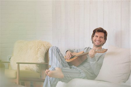 Smiling man in pajamas playing guitar in living room Stock Photo - Premium Royalty-Free, Code: 6113-08722084