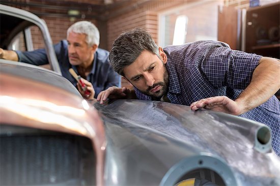 Focused mechanic examining classic car panel in auto repair shop Stock Photo - Premium Royalty-Free, Image code: 6113-08722248