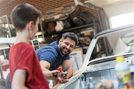 simsearch:6113-08722257,k - Smiling father taking tool from son in auto repair shop Photographie de stock - Premium Libres de Droits, Code: 6113-08722263