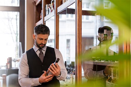 Well-dressed bartender examining whiskey bottle Photographie de stock - Premium Libres de Droits, Code: 6113-08722304