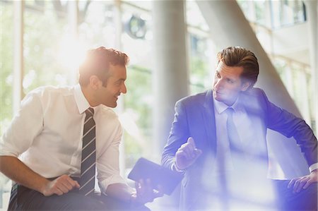 Businessmen talking and using digital tablet in sunny office lobby Photographie de stock - Premium Libres de Droits, Code: 6113-08882447