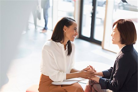 simsearch:614-07487041,k - Smiling businesswomen holding hands in sunny office lobby Stock Photo - Premium Royalty-Free, Code: 6113-08882453