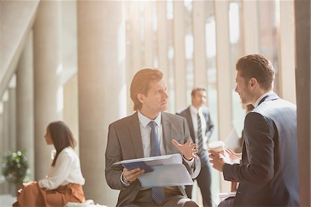 simsearch:6113-09058702,k - Businessmen discussing paperwork in sunny office lobby Stock Photo - Premium Royalty-Free, Code: 6113-08882505