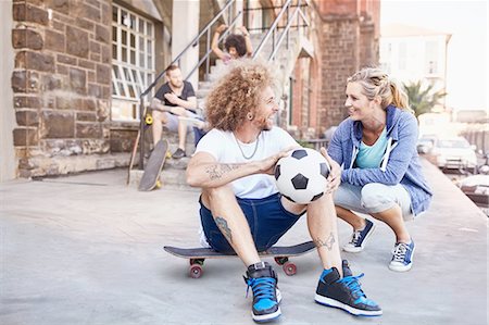 simsearch:6113-08882728,k - Smiling couple with soccer ball and skateboard talking on urban sidewalk Foto de stock - Royalty Free Premium, Número: 6113-08882750