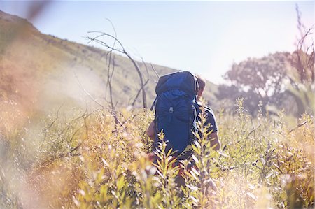 simsearch:841-07202269,k - Young man with backpack hiking in sunny field Photographie de stock - Premium Libres de Droits, Code: 6113-08882832