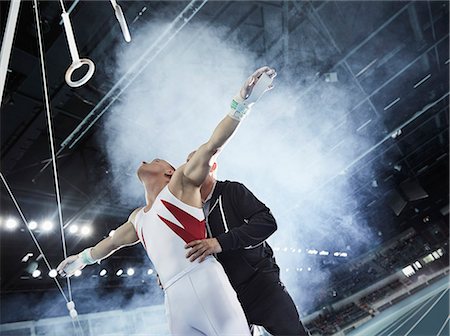 simsearch:632-05759894,k - Coach lifting male gymnast below gymnastics rings in arena Foto de stock - Sin royalties Premium, Código: 6113-08805461