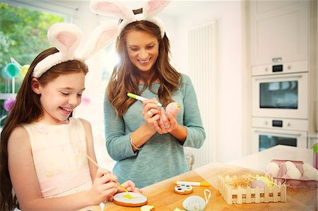 Mother and daughter wearing costume rabbit ears coloring Easter eggs and cookies Photographie de stock - Premium Libres de Droits, Code: 6113-08805662