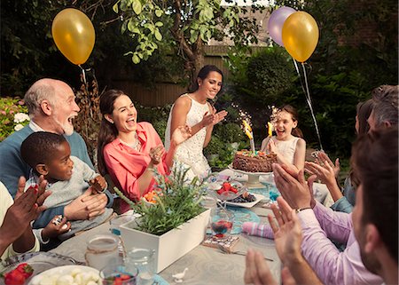 Multi-ethnic multi-generation family clapping celebrating birthday with fireworks cake at patio table Foto de stock - Sin royalties Premium, Código: 6113-08805685