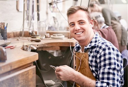 Portrait smiling male jeweler working listening to music with headphones in workshop Stock Photo - Premium Royalty-Free, Code: 6113-08805720