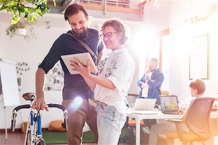 Smiling design professionals with bicycle and digital tablet talking in office Stock Photo - Premium Royalty-Free, Code: 6113-08805860