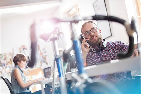 simsearch:6113-08882839,k - Bicycle leaning against desk next to male design professional talking on cell phone in office Foto de stock - Royalty Free Premium, Número: 6113-08805898