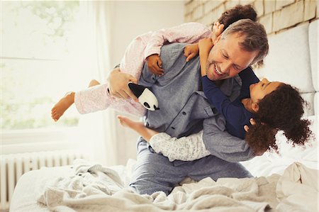 simsearch:6113-07242297,k - Multi-ethnic daughters playing and tackling father on bed Stock Photo - Premium Royalty-Free, Code: 6113-08943571
