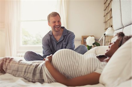 Multi-ethnic pregnant couple relaxing and laughing on bed Stock Photo - Premium Royalty-Free, Code: 6113-08943574