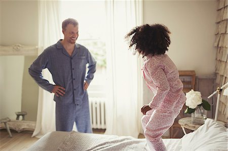 Multi-ethnic father in pajamas watching daughter jumping on bed Stock Photo - Premium Royalty-Free, Code: 6113-08943590