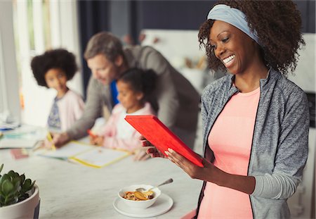 Smiling mother using digital tablet and eating breakfast in kitchen with young family Stock Photo - Premium Royalty-Free, Code: 6113-08943647