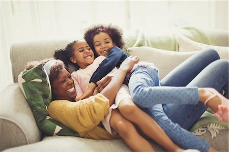 Playful mother and daughters cuddling on sofa Foto de stock - Sin royalties Premium, Código: 6113-08943644