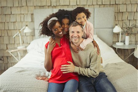 Portrait enthusiastic pregnant young family hugging on bed Stock Photo - Premium Royalty-Free, Code: 6113-08943623