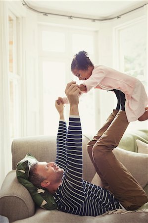 simsearch:6113-07147767,k - Multi-ethnic father playing, balancing daughter on legs overhead on sofa Photographie de stock - Premium Libres de Droits, Code: 6113-08943630