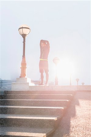 simsearch:6113-08943763,k - Male runner stretching arms at sunny urban lamppost Photographie de stock - Premium Libres de Droits, Code: 6113-08943765