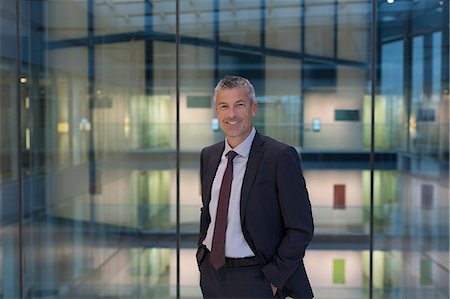 successful businessman standing photo - Portrait smiling, confident businessman in modern office atrium Stock Photo - Premium Royalty-Free, Code: 6113-08943787