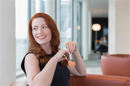 simsearch:6108-05868342,k - Smiling businesswoman with red hair looking over shoulder in lounge Photographie de stock - Premium Libres de Droits, Code: 6113-08943716